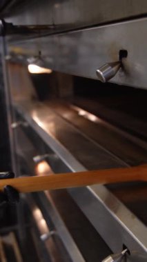 Baker taze pişmiş ekmeği fırından çıkarır. Sıcak somunlar, geleneksel pişirme süreci. Küçük fırın ayarları.