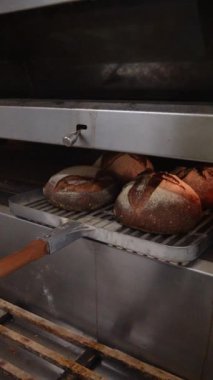 Baker taze pişmiş ekmeği fırından çıkarır. Sıcak somunlar, geleneksel pişirme süreci. Küçük fırın ayarları.
