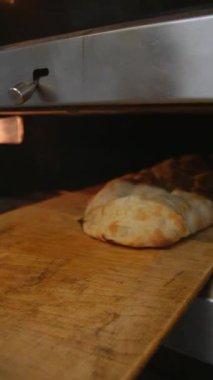 Baker taze pişmiş ekmeği fırından çıkarır. Sıcak somunlar, geleneksel pişirme süreci. Küçük fırın ayarları.