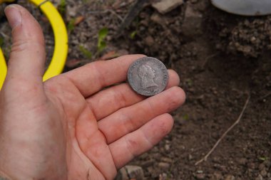 Metal dedektörüyle hazine avı. Bir tarafında antik bir hükümdarın portresi, diğer tarafında da nane izinin olduğu bir madeni paranın yakın çekimi. Bir hazine avcısının elindeki antik para..