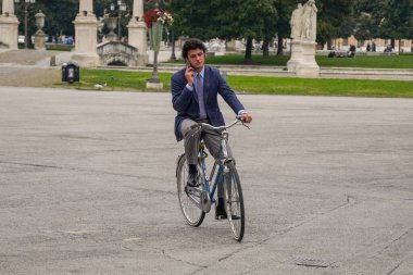 Roma 'nın göbeğinde bisiklet süren zarif bir adam. Klasik takım elbiseli bir adam şık bir şehir bisikleti sürüyor. Görüntü, zarafet ve tarzın bir kombinasyonunu iletir. Roma 14.04.2025