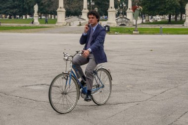 Roma 'nın göbeğinde bisiklet süren zarif bir adam. Klasik takım elbiseli bir adam şık bir şehir bisikleti sürüyor. Görüntü, zarafet ve tarzın bir kombinasyonunu iletir. Roma 14.04.2025