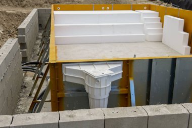 Çelik bir yüzme havuzu inşaatı. Çerçevenin dibi beton ve teknik bir deliği var. Beyaz modüler bloklar yerleştirilerek merdiven ve dinlenme alanları oluşturuldu.