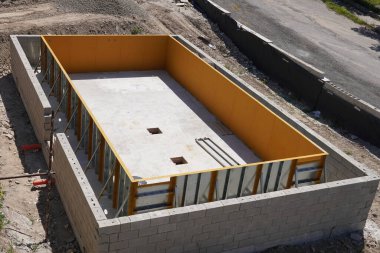 Çelik bir yüzme havuzu inşaatı. Çerçevenin dibi beton ve teknik bir deliği var. Beyaz modüler bloklar yerleştirilerek merdiven ve dinlenme alanları oluşturuldu.