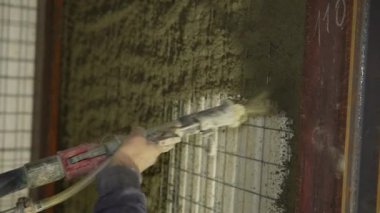 Tüfek başvurusu. İşçi elinin kapalı çekim pnömatik nozül püskürtme polistiren paneller üzerine bir katman av tüfeği spreyi tel örgü bağlı. Polistiren yalıtımlı ev.