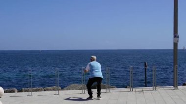 Denizin kenarında sabah egzersizi. Her yaştan insan güney İtalya şehrindeki gezinti güvertesinde bacaklarını açar. Palermo, Sicilya 04.05.2025