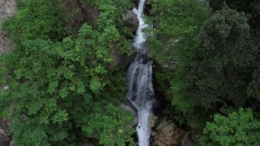 Şelale Şelalesi. Dağ Peçesi Fısıltısı. Bu nefes kesen dron görüntüsü dağların ortasındaki yoğun bir ormanın derinliklerinde çağlayan bir şelale gösteriyor..
