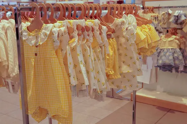 Butikte çocuk kıyafetleri. Yeni doğan erkek ve kızlar için düzenli bir elbise rafı. Sette pantolon, gömlek ve çizgili ve düğmeli bir tulum var. Hepsi de ahşap askılarda..