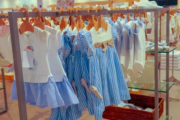 Kız Giysileri - Mavi ve Beyaz Elbiseler Sevimli kızlar bir butikte ahşap askılarda giyinirler