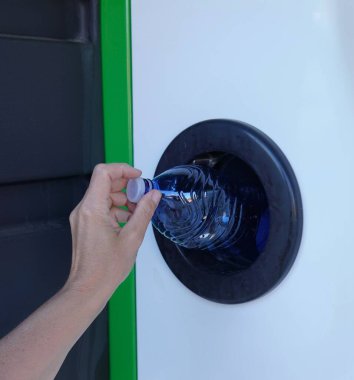 Şişeleri plastik geri dönüşüm makinesine geri vermek. Çevresel sorumluluğun gösterimi ve yenilikçi atık geri dönüşüm çözümleri. Plastik şişeyi makineye sokan kişinin yakın plan fotoğrafı.