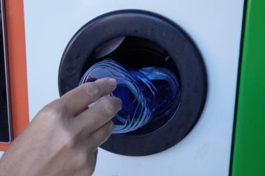 Şişeleri plastik geri dönüşüm makinesine geri vermek. Çevresel sorumluluğun gösterimi ve yenilikçi atık geri dönüşüm çözümleri. Plastik şişeyi makineye sokan kişinin yakın plan fotoğrafı.
