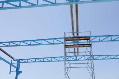 Çelik bir yapı kuruyorum. Çelik bir yapının inşa edildiği bir inşaat alanı. Ağır zincirleri olan bir vinç. İskele işçilere destek sağlıyor. Parlak mavi ve endüstriyel manzara.