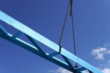 Çelik bir yapı kuruyorum. Çelik bir yapının inşa edildiği bir inşaat alanı. Ağır zincirleri olan bir vinç. İskele işçilere destek sağlıyor. Parlak mavi ve endüstriyel manzara.