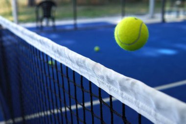 Ekipmanlı Padel kortu. Ortasında ağ olan parlak mavi bir padel kortu. Parlak sarı toplar yüzeye saçıldı ve özel padel raketler yakına yerleştirildi..