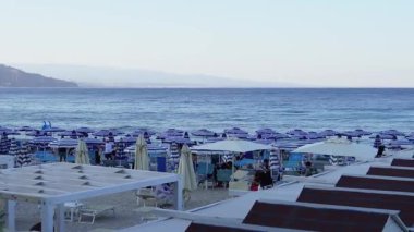 Akdeniz sahilinin havadan görünüşü. Güney İtalya 'da bir sahil şeridi. Sıralar dolusu şemsiye ve güneş şezlongları deniz kıyısındaki bir tatil beldesinin altın kumları arasında. Kristal berrak deniz, küçük dalgalar