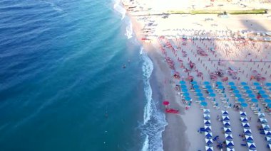 Akdeniz sahilinin havadan görünüşü. Güney İtalya 'da bir sahil şeridi. Sıralar dolusu şemsiye ve güneş şezlongları deniz kıyısındaki bir tatil beldesinin altın kumları arasında. Kristal berrak deniz, küçük dalgalar