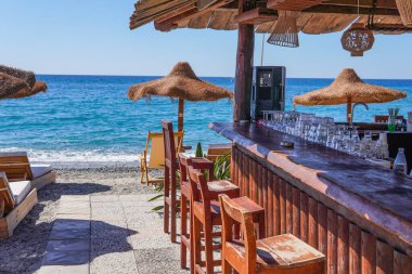 Palmiye ağaçları, sahil barı, deniz kenarında güneş pansiyonları ve şemsiyeleri olan tropik bir sahil. Güney sahilinde yaz tatili.