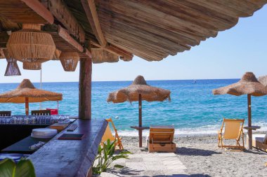 Palmiye ağaçları, sahil barı, deniz kenarında güneş pansiyonları ve şemsiyeleri olan tropik bir sahil. Güney sahilinde yaz tatili.