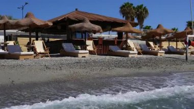 Palmiye ağaçları, sahil barı, deniz kenarında güneş pansiyonları ve şemsiyeleri olan tropik bir sahil. Güney sahilinde yaz tatili.