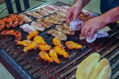 V şeklinde ızgaralı paslanmaz çelik ızgaranın yakın çekimi. Sosisler ve pancetta cızırdıyor, ve yağ damlıyor, sıcak kırmızı kömürlerin üzerinde tütüyor. Parlak, iştah açıcı bir ızgara sahnesi..