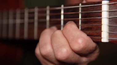 Çalarken tellere basan bir gitaristin yakın çekimi. Parmakları, canlı bir müzikal performansın yoğunluğunu ve duygusunu aktararak tam ve ritmik bir şekilde hareket eder..