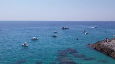 İnsansız hava aracı bir deniz mağarasında uçarak turkuaz su, tekne, yelkenli, yaz tatili atmosferi, dinlenen turistler, İtalya 'nın güney sahillerindeki güneşli tatil atmosferini gözler önüne seriyor.