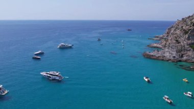 Su üzerinde yüzüyor gibi görünen turkuaz deniz, tekne ve yatlar, pedal süren turistler ve çarpıcı bir Akdeniz cennetinde keyif teknelerine binen turistler.