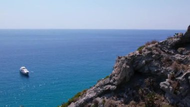 Turkuaz deniz manzarası, sudaki granit kayalar, suyun üzerinde süzülen tekne ve yatlar, pedal süren turistler ve çarpıcı bir Akdeniz cennetinde keyif tekneleri.