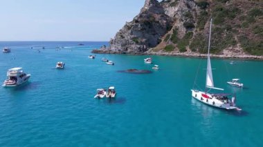 Su üzerinde yüzüyor gibi görünen turkuaz deniz, tekne ve yatlar, pedal süren turistler ve çarpıcı bir Akdeniz cennetinde keyif teknelerine binen turistler.