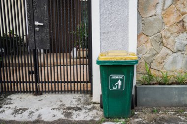 Evin ön çitindeki yeşil çöp tenekesi.