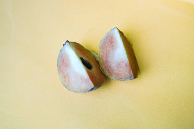Sarı arka planda izole edilmiş olgun sapodilla meyvesi. Dilimlenmiş taze sapodilla