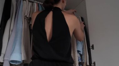 Kıyafetini seçen genç bir kadın. İş için kıyafet ya da önemli bir olay seçiyor. Güven ve profesyonelliği yansıtmak amacıyla giyiniyor.