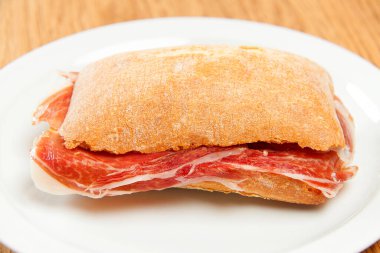 Beyaz tabakta serrano jambonlu mini sandviç ve ciabatta ekmeği ve ahşap arka plan.