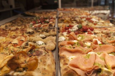 Çeşitli pizza dilimleriyle restoran vitrininde. Ürünleri ve baharatları görebilirsiniz.