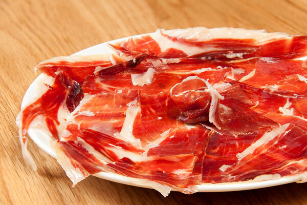 Fragment of plate with slices of Serrano ham in circular formation on wooden background