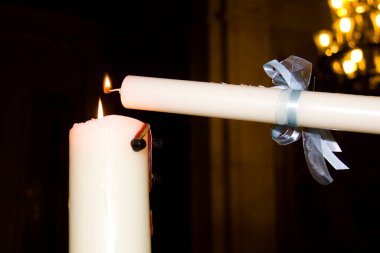 İki mum, alevlerini karanlık arka planda bir kilise ortamında paylaşmak için bir araya geldi.
