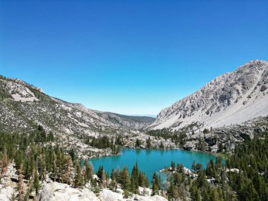 Inyo Ulusal Ormanı 'ndaki patikalar, John Muir Wilderness, güneşli bir günde dağ gölü, dağların arkasındaki dağ ormanları ve berrak bir göl, bulutsuz bir gökyüzüne karşı turkuaz göl.
