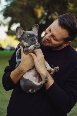 Bir adam köpeğe sarılıyor, parkta yürüyor, sahibi olan Fransız buldog köpeğinin dışında, evcil hayvanıyla evin dışında vakit geçiren bir erkek, mutlu bir köpekle gülümseyen insanlar.