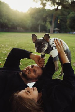 Parkta köpekle gezen bir aile, parkta tasmayla dolaşan bir buldog yavrusu, evin dışında evcil hayvan vakit geçiren genç bir çift.