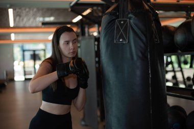 Boks eldivenli bir kadın spor salonunda kum torbasına vurur, kadın antrenman yapar, boks yapar, kardiyo egzersizleri yapar yağ yakar, güç ve dayanıklılık kazanır, esmer kız boks yapmayı öğrenir.