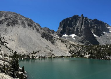 Inyo Ulusal Ormanı 'ndaki patikalar, John Muir Wilderness, güneşli bir günde dağ gölü, dağların arkasındaki dağ ormanları ve berrak bir göl, bulutsuz bir gökyüzüne karşı turkuaz göl.