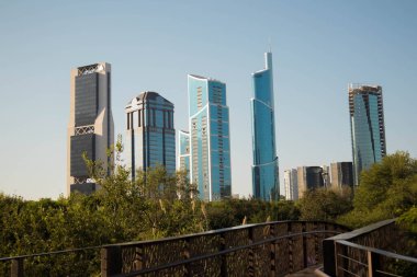 A striking view of San Pedro Garzas modern skyline from Rufino Tamayo Park, with trees and a bridge in the foreground under a clear blue sky clipart