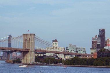Manhattan 'dan Brooklyn Köprüsü manzaralı, ikonik Clocktower binası DUMBO, Brooklyn' de. Modern ve tarihi mimari gökyüzünün altındaki ufuk çizgisini çerçevelerken gemiler Doğu Nehri 'nde geziniyor.
