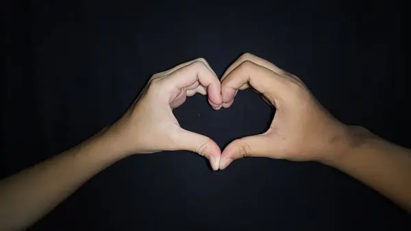 Bir kalp oluşturan iki sevgili eli. Siyah arka planda izole edilmiş.