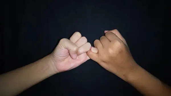 İki el ve bir jest. Küçük parmağın umudunu gösteriyor. Siyah arka planda izole edilmiş.