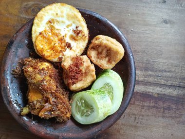 Ayam Goreng Lalapan. Ahşap masa üzerinde kızarmış tavuk, tofu, yumurta ve sebzeler.