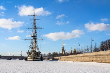 Tarihi bir gemiyle donmuş Neva Nehri 'nin kış manzarası ve Rusya' nın Saint Petersburg kentindeki Peter ve Paul Kalesi. Açık mavi gökyüzü, karlı manzarayla ve ünlü simgelerle çelişiyor.