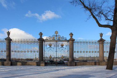 Saint Petersburg, Rusya 'daki Summer Garden' daki süslü çitlerin kış manzarası. Tarihsel dövülmüş demir kapı karlı bir araziye ve parlak mavi gökyüzüne karşı duruyor.