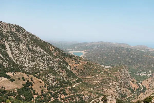 Lassithi Platosu Serpentine yolunu, Agios Konstantinos 'u küçük su deposunu ve çevresindeki yeşillikleri görüyor.