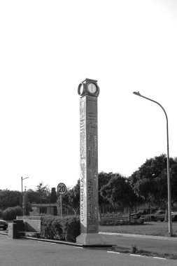 Paphos, Cyprus- 4 Eylül 2023: Roloi Pafou, Arkeoloji Parkının girişinde uzun bir metal saat ve deniz kenarında siyah-beyaz gezinti alanı.